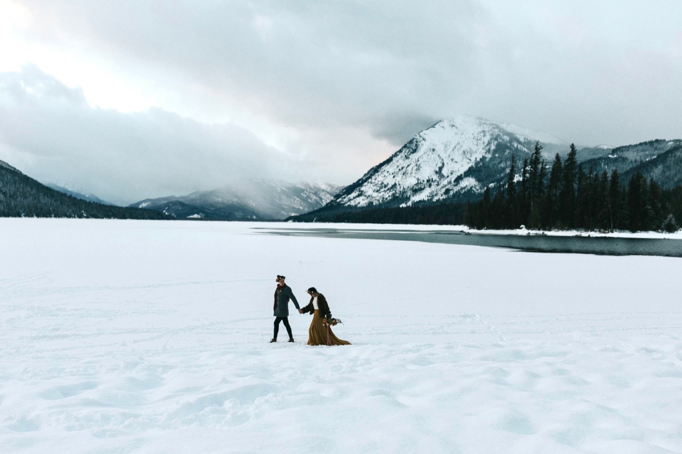 A couple on a snowy frozen lake below winter mountains