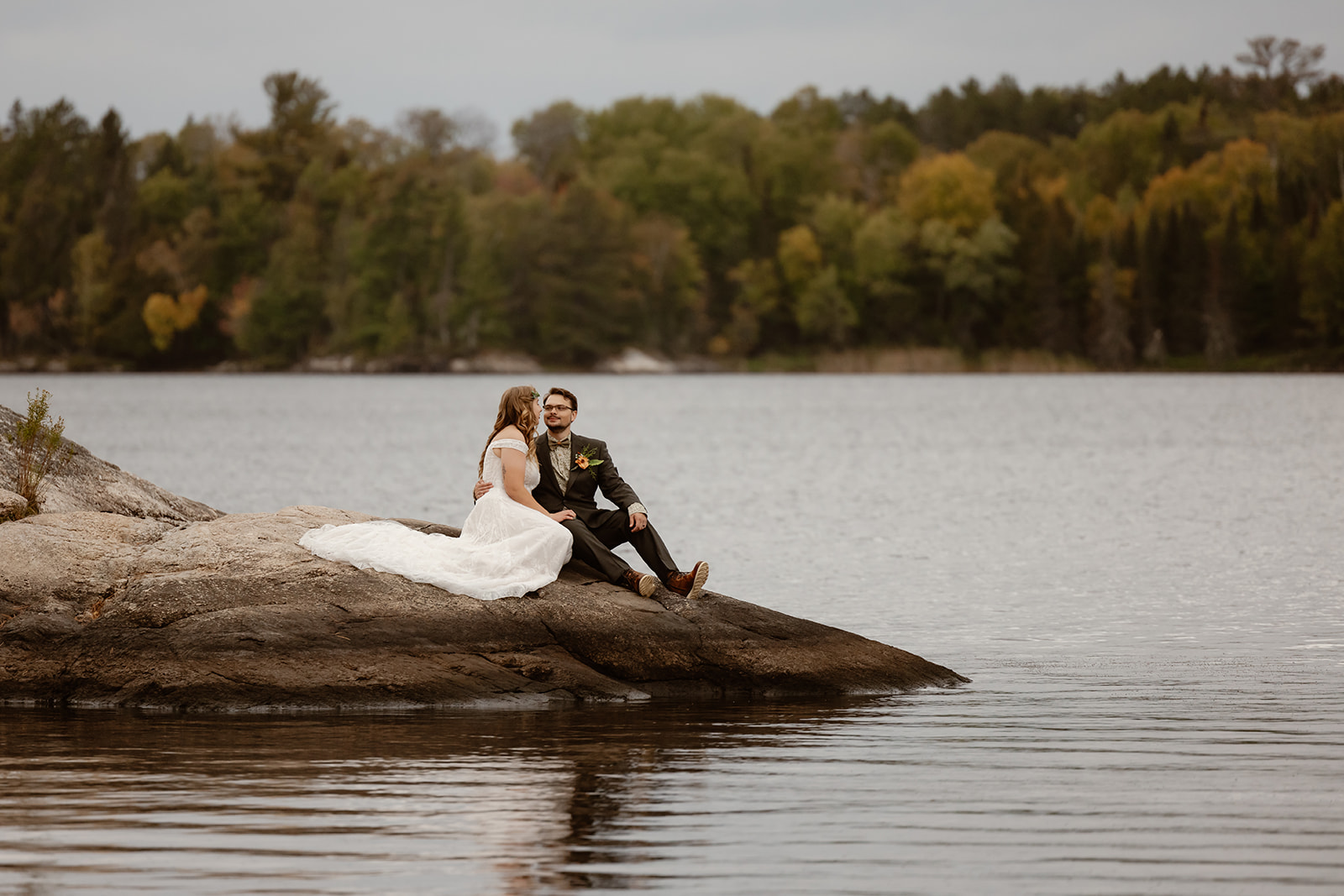 Couple sitting on a granite rock surrounded by lake water at a Voyageurs National Park elopement