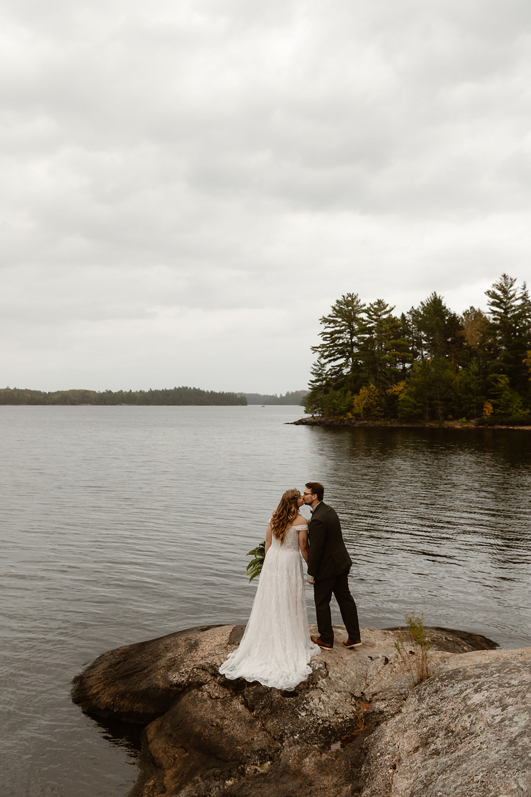 Couple kissing at the edge of the lake with a pine island behind them at a Voyageurs National Park elopement